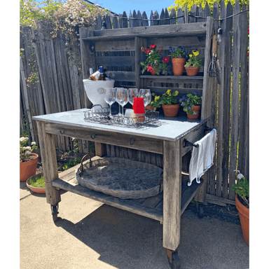 Outdoor wooden table with drinks and plants against a wooden fence.