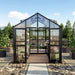 Front view of the Vego Garden Victorian Greenhouse with glass walls, black frame, double doors and paved garden walkway