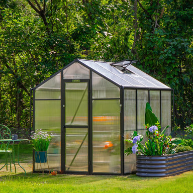 Vego Junior Victorian 6.5ft wide greenhouse with black aluminum frame, gable roof and single door in a landscaped backyard.