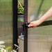 Close-up of a hand opening the Vego Junior Victorian Greenhouse hinged door with black handle and translucent polycarbonate panels