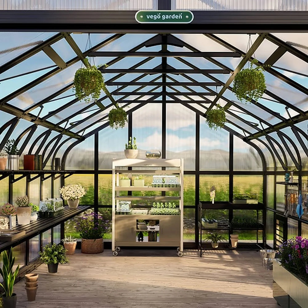 greenhouse interior with growing benches, a central work table and hanging planters beneath the roof.